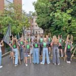 Les élèves de 6e, vus de dos, avec leurs échasses et le drapeau de l'école avant la Joute des enfants